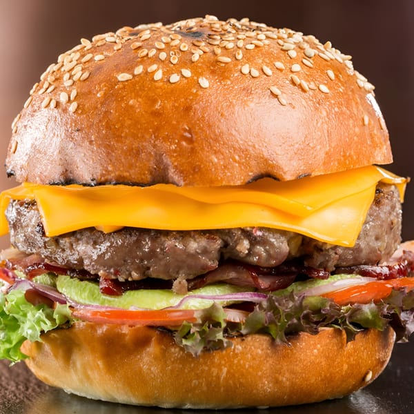 Close-up of a Fresh Horses Saloon burger with cheese, lettuce, tomato, onion, and bacon.