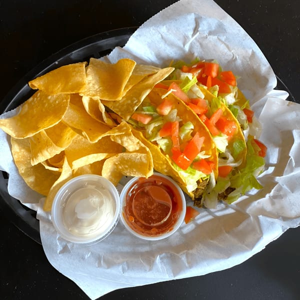 Two Fresh Horses Saloon tacos with chips, salsa, and sour cream in a black basket.