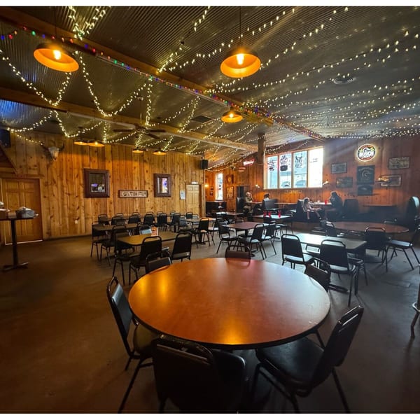 Rustic interior of Fresh Horses Saloon with wooden walls, string lights, and scattered tables and chairs.