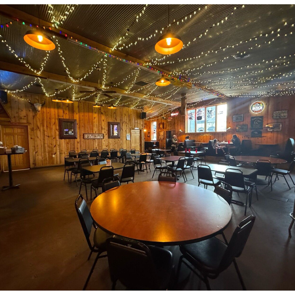 Rustic interior of Fresh Horses Saloon with wooden walls, string lights, and scattered tables and chairs.